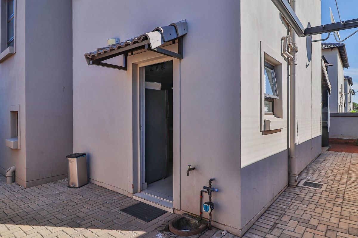 Rear exterior view of the townhouse featuring a paved courtyard, external water tap, and a small tiled awning over the doorway.
