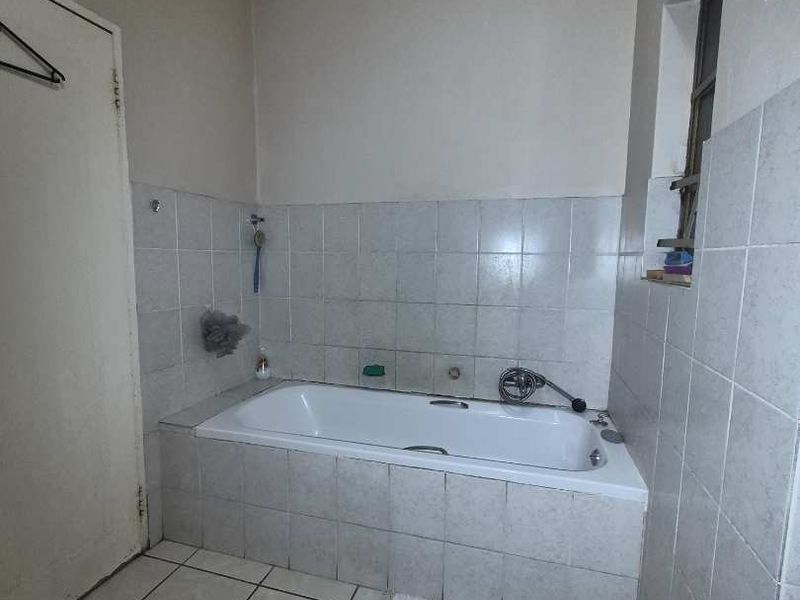 A functional bathroom featuring a built-in bathtub with tiled surround and flooring, offering a clean and simple layout ready for potential cosmetic updates.