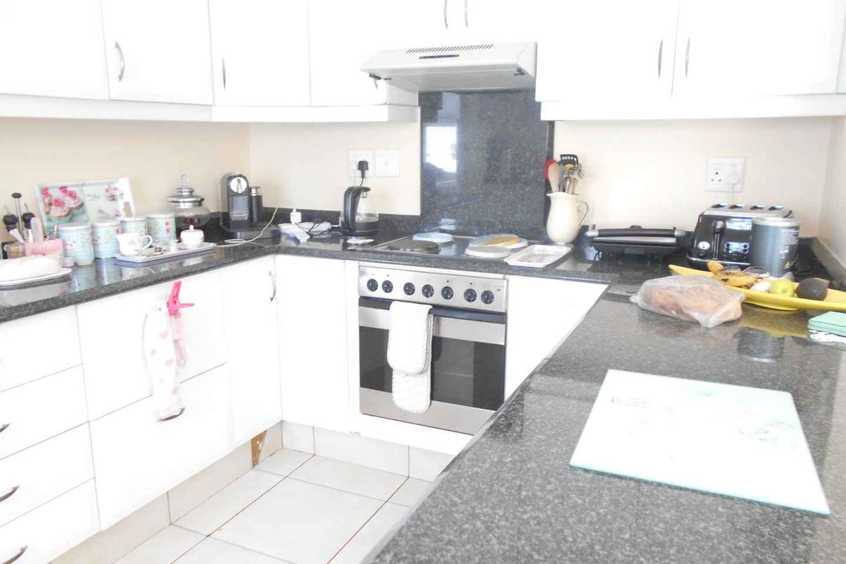 Functional kitchen featuring white cabinetry, granite countertops, and built-in electric oven and hob with extractor fan.