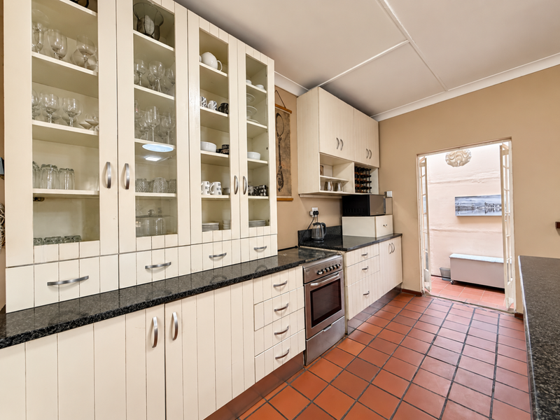 A functional kitchen featuring extensive built-in cabinetry with glass display sections, granite countertops, a freestanding oven, and direct access to an outdoor patio area.