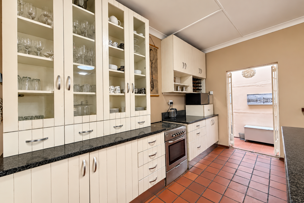 A functional kitchen featuring extensive built-in cabinetry with glass display sections, granite countertops, a freestanding oven, and direct access to an outdoor patio area.