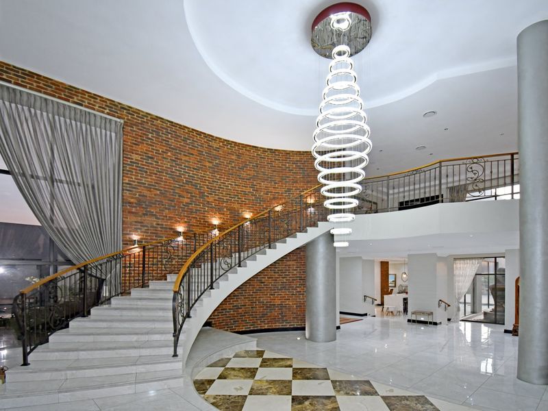 Grand entrance hall featuring a sweeping curved staircase, exposed brick wall, polished marble flooring, and a striking modern chandelier.