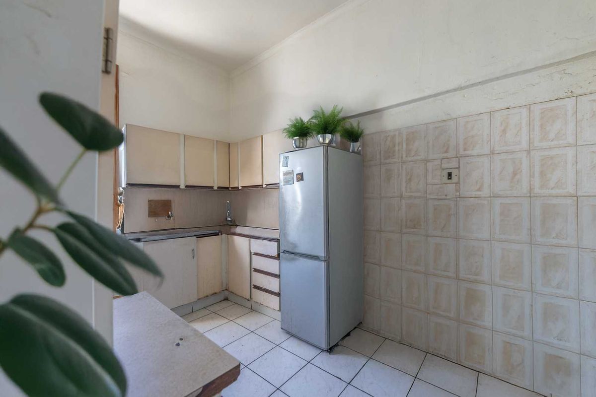 A compact kitchen featuring dated cabinetry, tiled walls, and floor tiles, offering a functional layout ready for modernization and renovation.