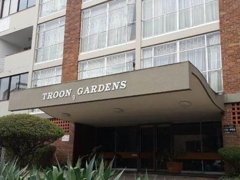Front entrance view of Troon Gardens apartment building, featuring a prominent concrete canopy, brick facade, and large multi-pane windows.