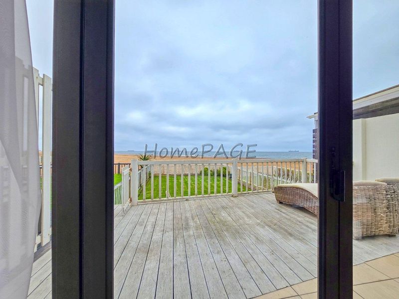 A timber deck patio overlooking the ocean, featuring a wooden balustrade and direct access through sliding glass doors.