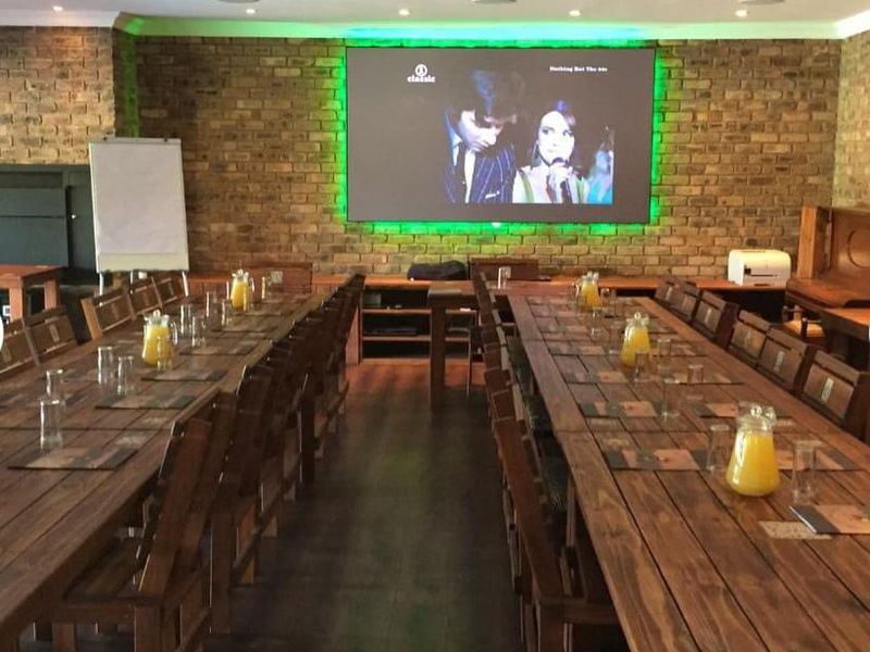A spacious entertainment or cinema room featuring exposed brick walls, recessed lighting, and a large projection screen setup, suitable for events or media viewing.
