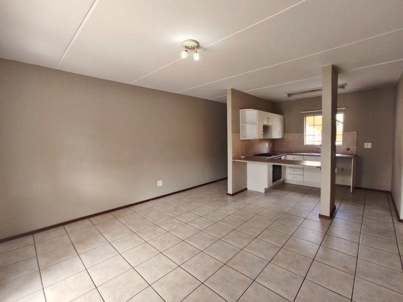 Spacious open-plan living area featuring tiled flooring and a functional kitchen with built-in cabinetry, oven, and hob.