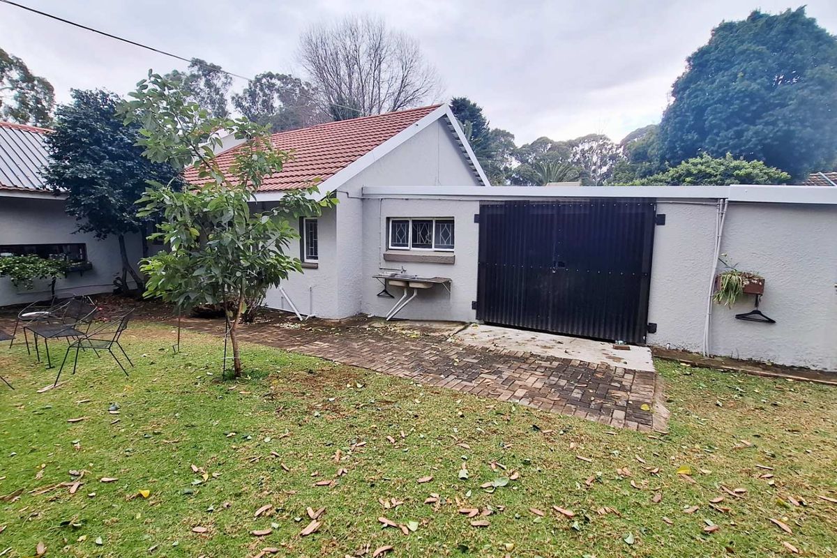 Rear view of the property featuring a paved walkway, lawn area, external wash basin, and a secure garage entrance.