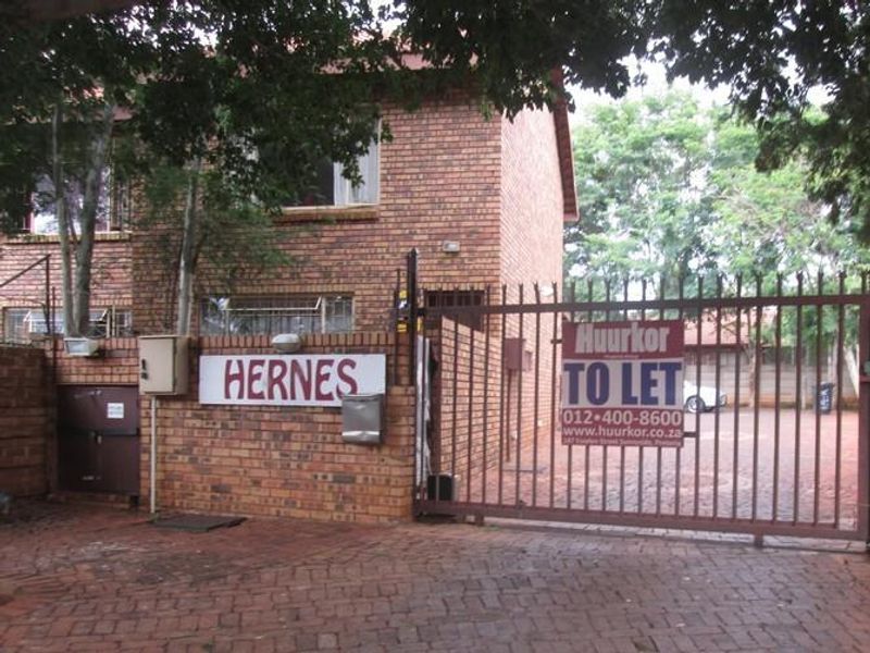 Front entrance view of the apartment complex featuring a brick facade, paved driveway, and secure metal gate access.