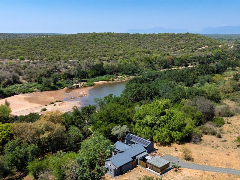 Aerial view of a property featuring a metal roof with solar panels, situated in a scenic natural landscape near a river.