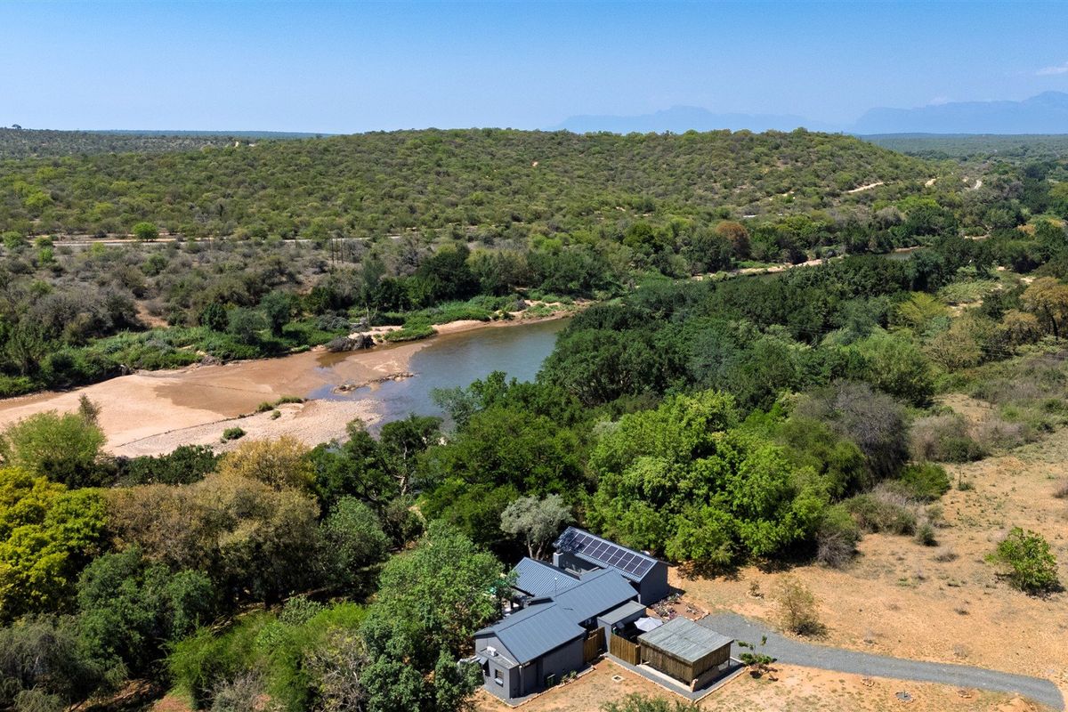 Aerial view of a property featuring a metal roof with solar panels, situated in a scenic natural landscape near a river.