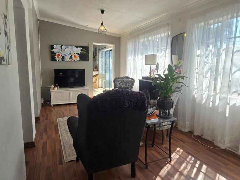 A cozy living room featuring laminate flooring, neutral wall tones, and large windows that allow for ample natural light.