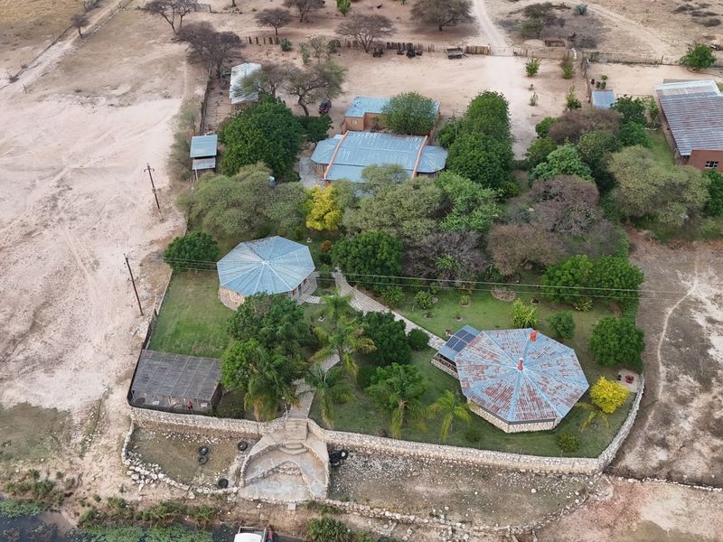 Aerial view of a small holding property featuring multiple structures with metal roofing, stone retaining walls, and established garden areas.