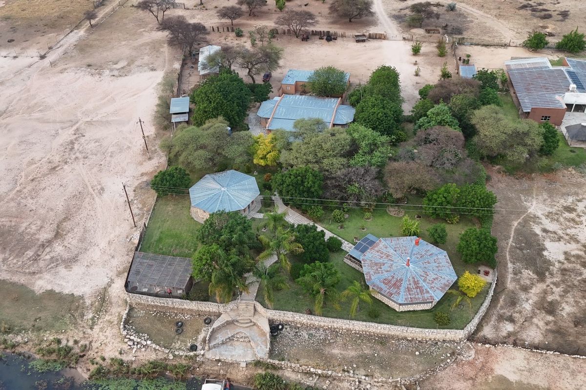 Aerial view of a small holding property featuring multiple structures with metal roofing, stone retaining walls, and established garden areas.