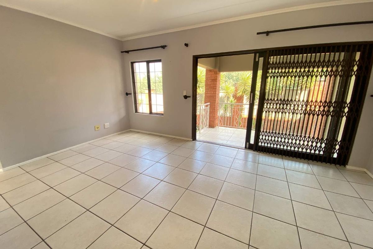 Spacious living area featuring neutral tiled flooring, large windows, and a sliding door providing direct access to a private balcony.