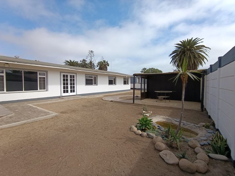 Rear exterior view featuring a covered patio area, paved walkways, a small garden pond, and a large enclosed yard with boundary walling.