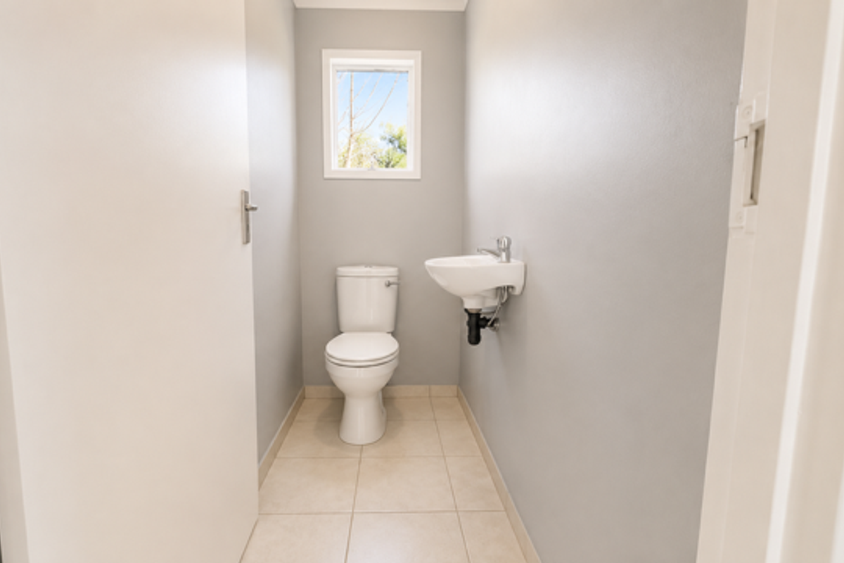A compact guest bathroom featuring a modern toilet and a wall-mounted basin with neutral tile flooring and light grey walls.
