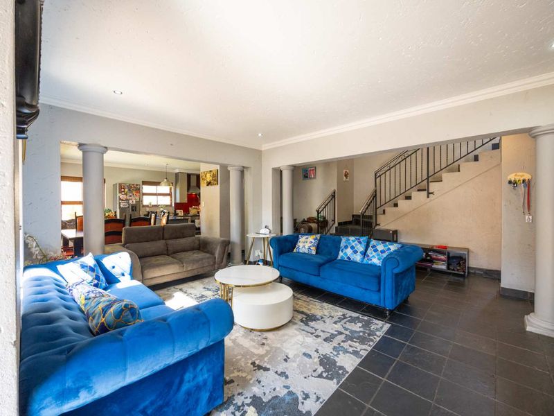 Spacious open-plan living area featuring tiled floors, decorative structural columns, and a staircase with a metal railing, seamlessly connecting to the kitchen space.