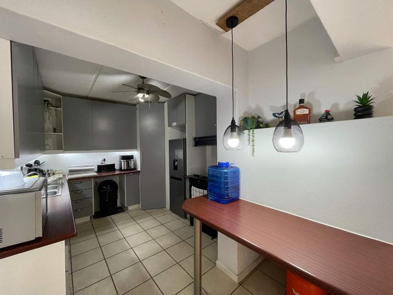 A functional kitchen featuring grey cabinetry, laminate countertops, tiled flooring, and a breakfast bar area with modern pendant lighting.