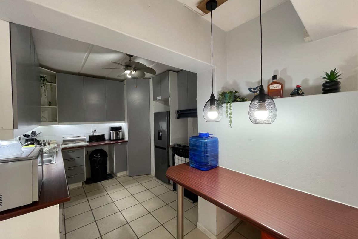 A functional kitchen featuring grey cabinetry, laminate countertops, tiled flooring, and a breakfast bar area with modern pendant lighting.