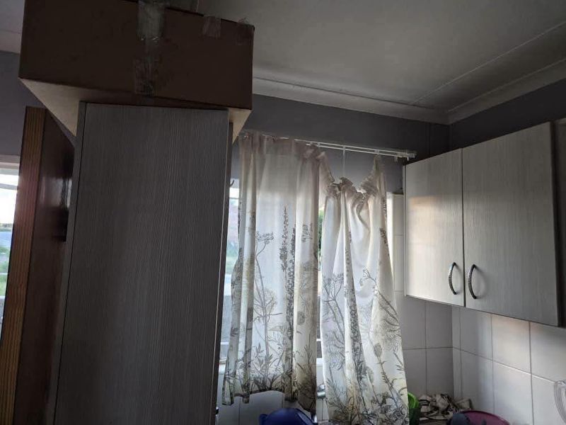 A kitchen area featuring built-in cabinetry and tiled splashbacks, currently showing signs of wear and an unfinished bulkhead section.