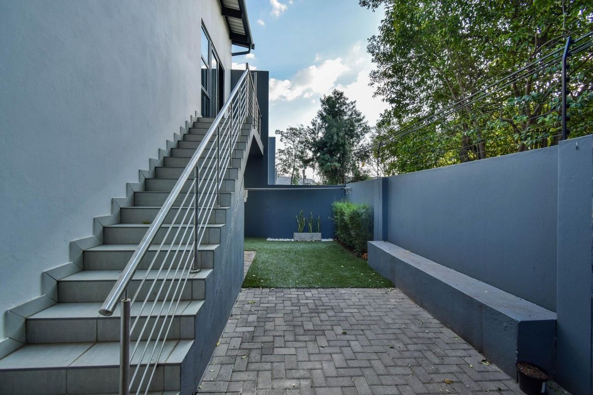 A private rear courtyard featuring paved flooring, a small artificial lawn area, and an external staircase with stainless steel railings leading to the upper level.