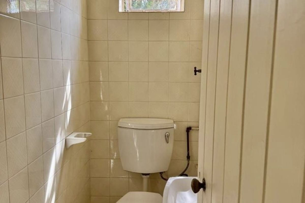 A compact, dated guest bathroom featuring ceramic wall and floor tiles, a standard toilet, and a small wall-mounted basin.