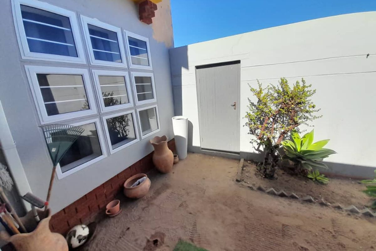 A rear exterior courtyard area featuring a paved wall section, multiple white-framed windows, and a solid access door.