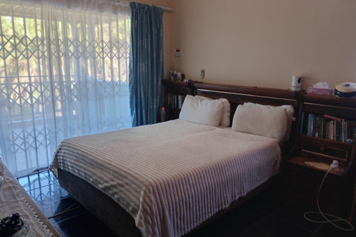 A bedroom featuring dark floor tiles, a built-in headboard with integrated shelving, and a sliding glass door with a security gate leading to the exterior.