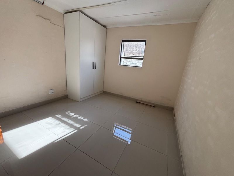 A compact, empty bedroom featuring tiled flooring, a built-in wardrobe, and a single window, requiring minor cosmetic repairs to walls and ceiling.