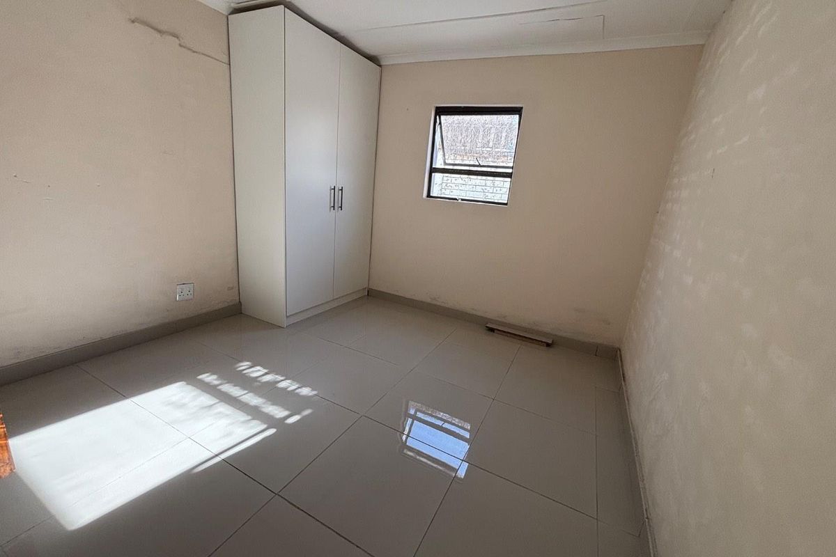 A compact, empty bedroom featuring tiled flooring, a built-in wardrobe, and a single window, requiring minor cosmetic repairs to walls and ceiling.