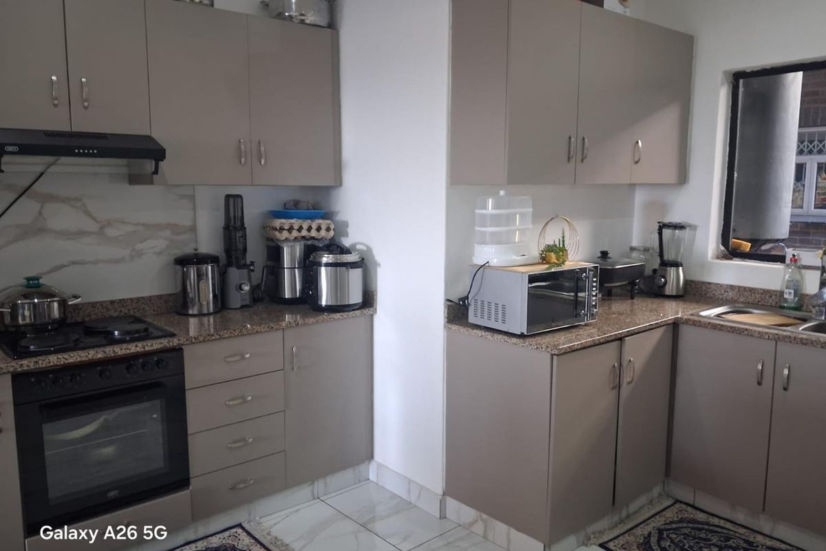 A functional kitchen featuring modern taupe cabinetry, granite countertops, a built-in oven with extractor fan, and tiled flooring.