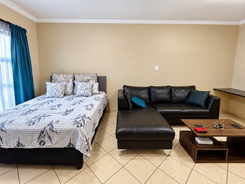A spacious bedroom featuring tiled flooring, crown molding, and a built-in desk area, offering a functional layout with neutral wall tones.