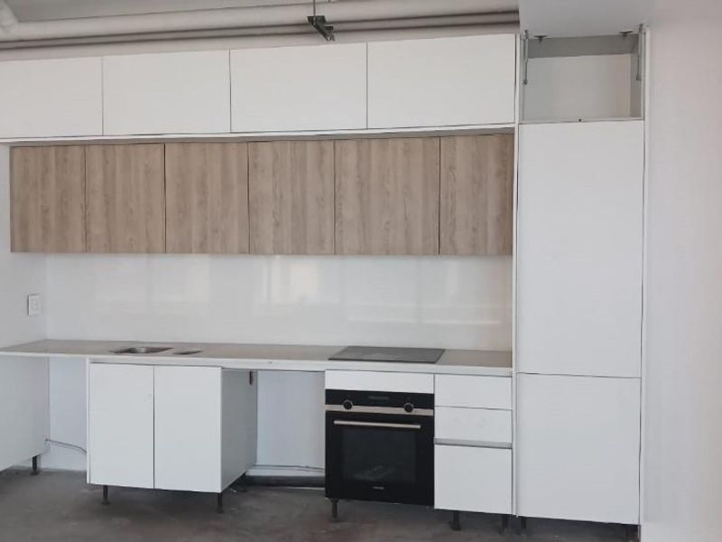 A modern kitchen featuring two-tone cabinetry, built-in oven, electric cooktop, and glass splashback, currently in an unfinished state awaiting final installation.