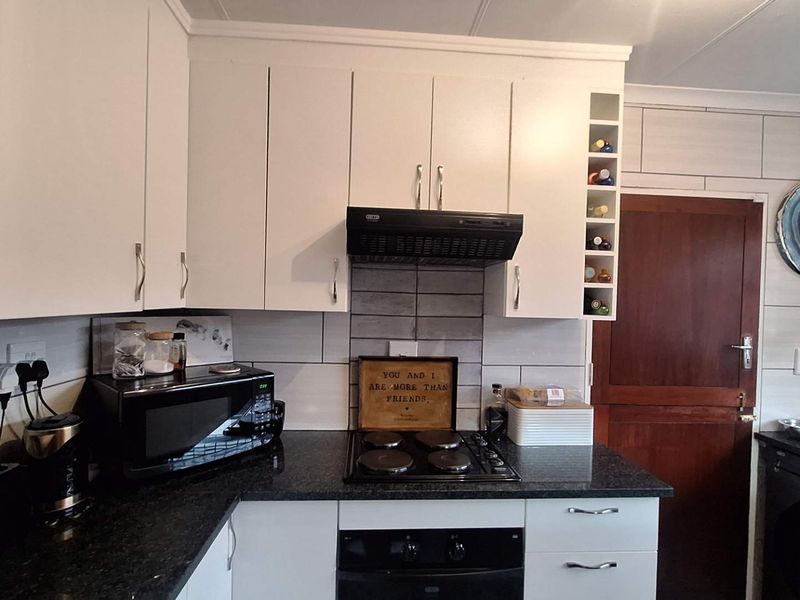 A functional kitchen featuring white cabinetry, dark granite countertops, a built-in oven and hob, extractor fan, and a tiled backsplash.