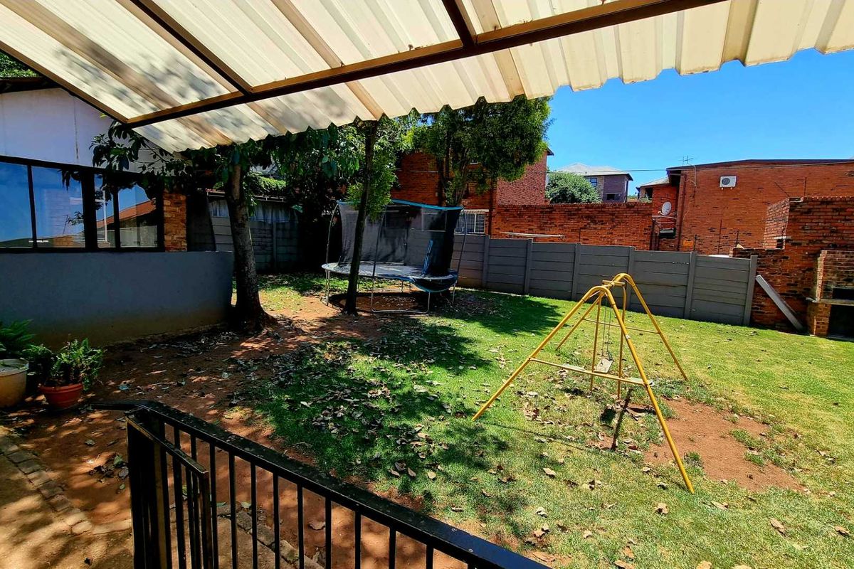 A private rear garden featuring a covered patio area, lawn, and a built-in brick braai, enclosed by perimeter walling.
