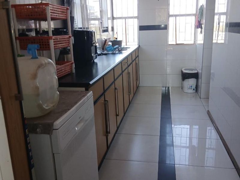 A functional scullery or utility area featuring built-in cabinetry, tiled flooring, and ample natural light through windows with security bars.