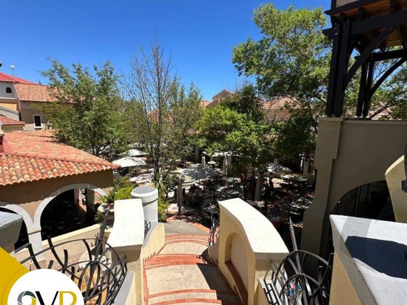An elevated view looking down a terracotta tiled staircase with wrought iron railings, leading towards a landscaped courtyard area with outdoor seating.