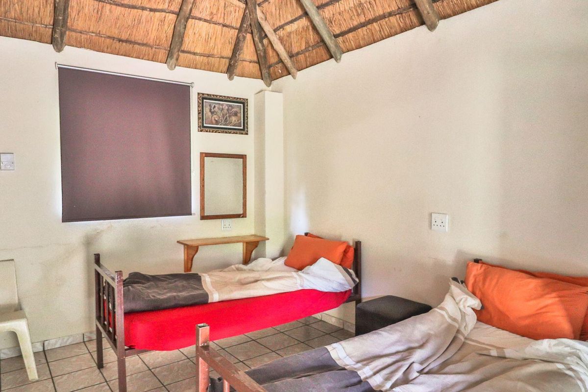A rustic bedroom featuring a traditional thatched roof, tiled flooring, and built-in wall-mounted shelving.