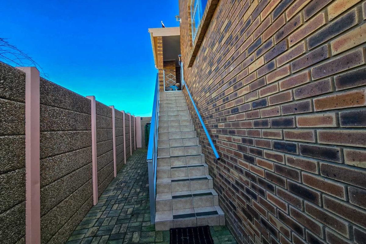 Exterior side passage featuring a brick facade, paved walkway, and a tiled staircase with a metal handrail leading to an elevated entrance.