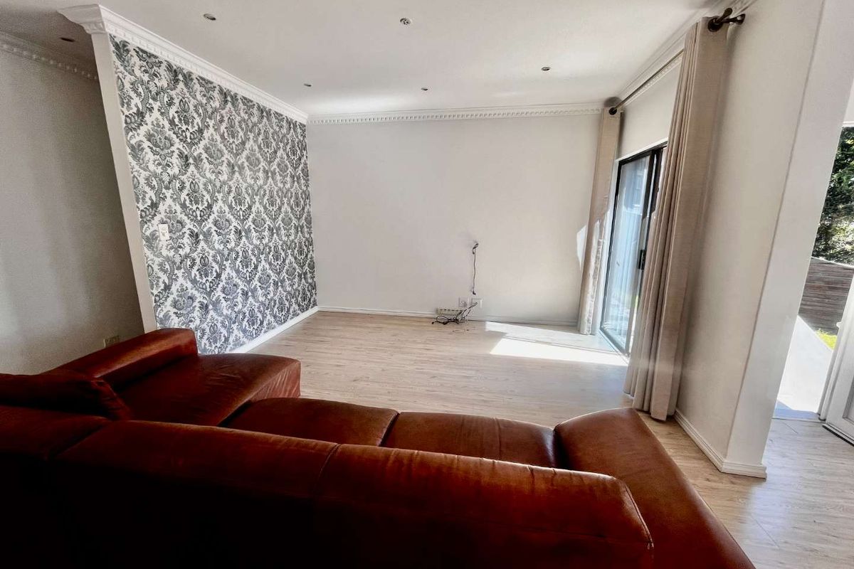 A bright living room featuring light wood-look flooring, decorative wallpaper, recessed ceiling lighting, and sliding glass doors providing access to the outdoor area.