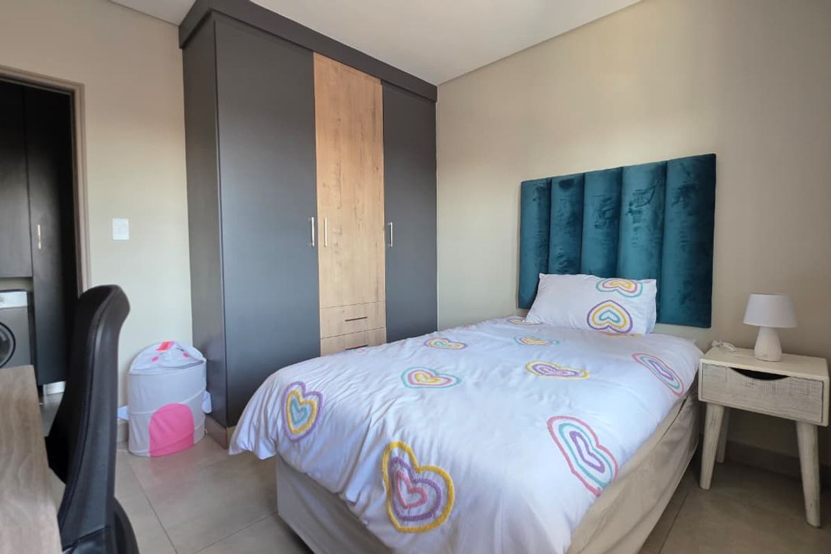 A well-maintained bedroom featuring modern built-in wardrobes with a two-tone finish and neutral tiled flooring.
