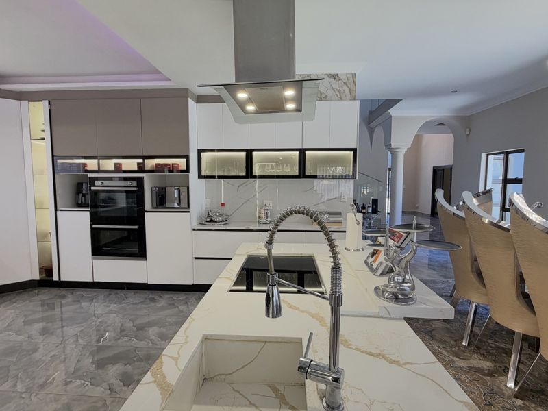 Modern open-plan kitchen featuring a large island with marble-look countertops, integrated appliances, sleek cabinetry, and high-end finishes throughout the space.