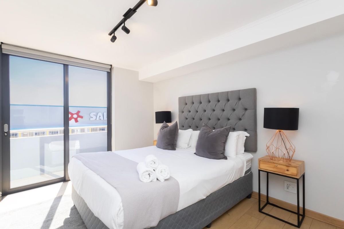 A modern bedroom featuring neutral tones, track lighting, and a large sliding glass door providing access to an outdoor area.