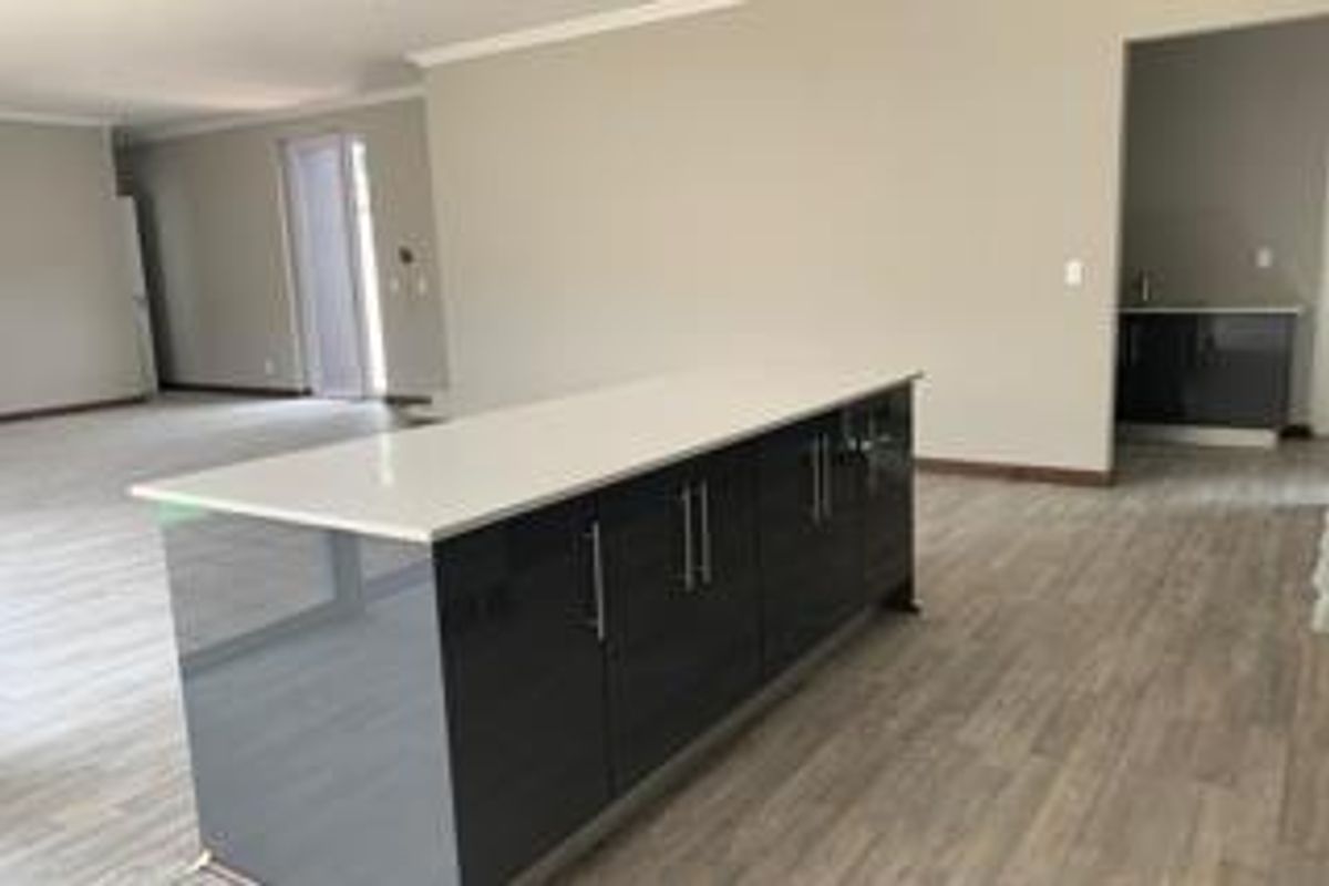 Spacious open-plan living area featuring a modern kitchen island with quartz countertops and sleek dark cabinetry, set against light-toned laminate flooring.