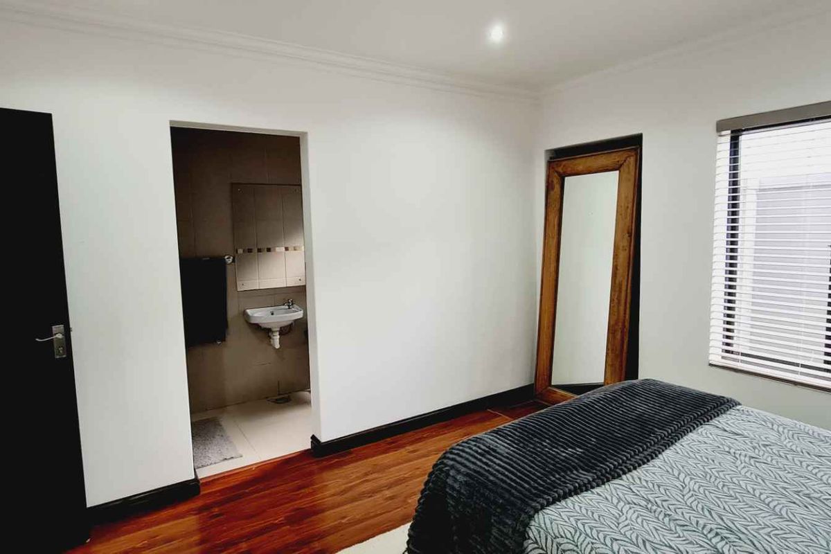 A well-maintained bedroom featuring warm hardwood flooring, venetian blinds, recessed lighting, and convenient access to an en-suite bathroom.