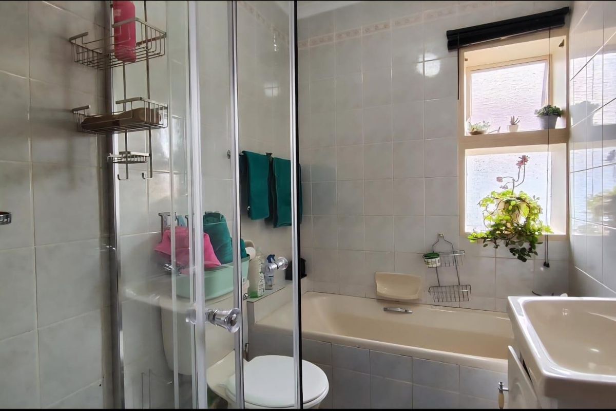 A functional bathroom featuring a combined shower and bathtub unit, a wall-mounted basin, and tiled walls with a window for natural light.