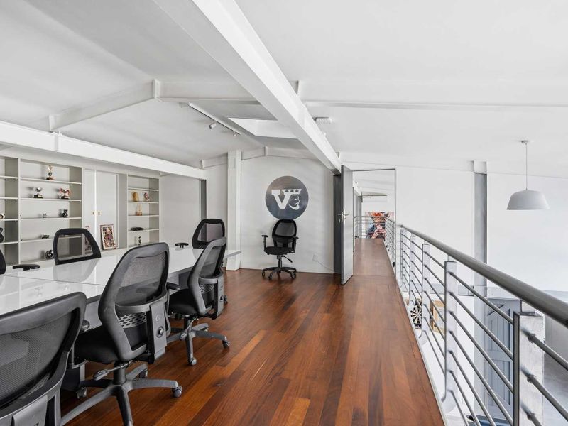 Modern mezzanine office space featuring polished hardwood flooring, exposed structural beams, built-in shelving, and natural light from overhead skylights.