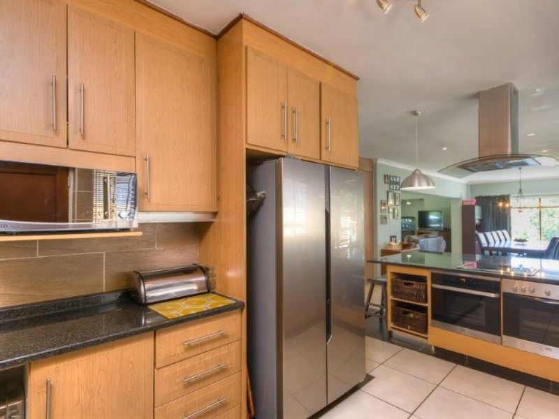 Open plan kitchen featuring light wood cabinetry, granite countertops, stainless steel appliances, and a central island, flowing into the adjacent dining and living area.