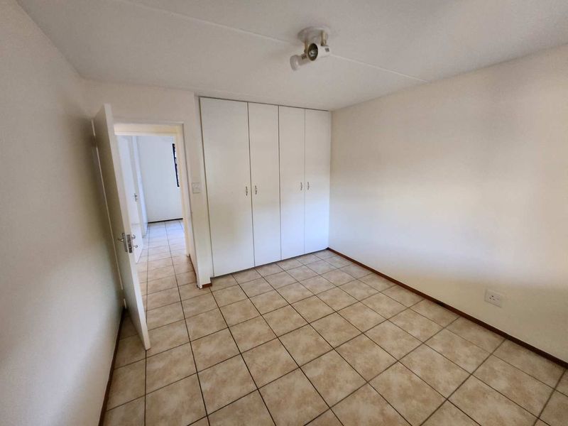 A clean, empty bedroom featuring neutral tiled flooring and ample built-in cupboard storage, offering a blank canvas for personalization.